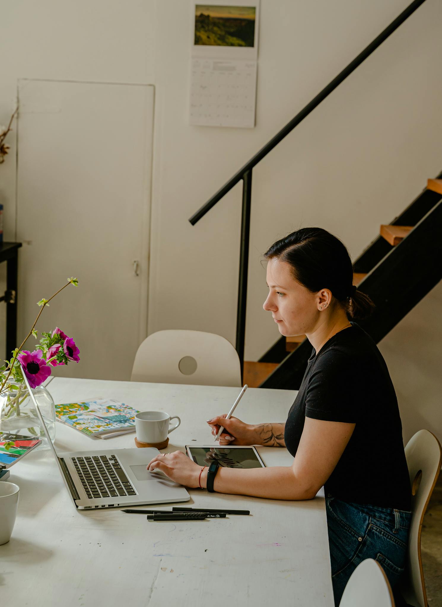 Woman using a digital pen with her laptop in a creative workspace featuring art materials.